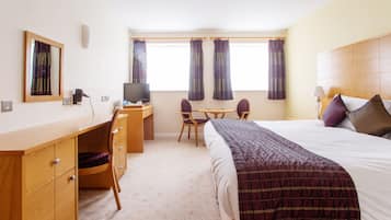 A hotel room with a bed, desk, chair, television, and curtains.