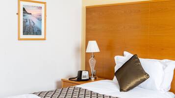 Una cama bien hecha con una colcha estampada, una lámpara de noche, un teléfono y un cuadro en la pared.