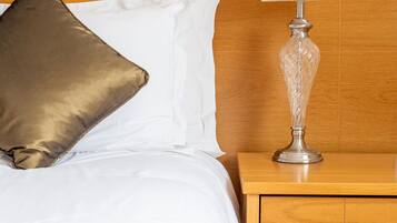 A neatly made bed with a patterned bedspread, a gold accent pillow, and a white pillow. A bedside table with a lamp and a drawer is visible.