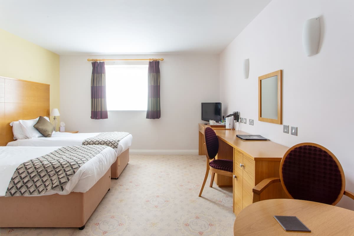 A hotel room with two beds, a desk, a chair, a television, and a window with curtains.