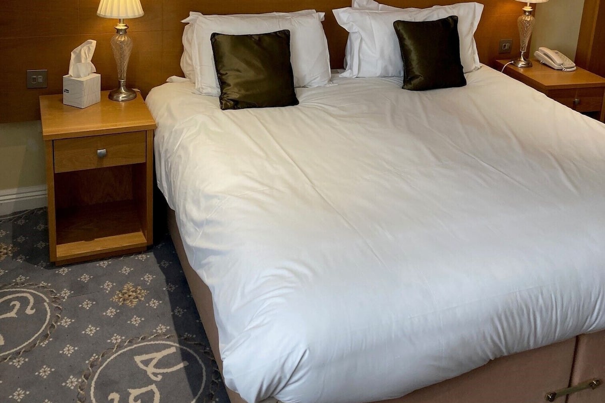 A hotel room with a large bed, two bedside tables, a wooden headboard, and a carpet with a circular pattern.