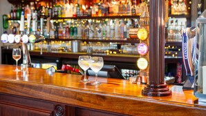 A bar area with a wooden counter, multiple illuminated drink dispensers, and a variety of bottles in the background. - George Albert Hotel & Spa (Dorchester)