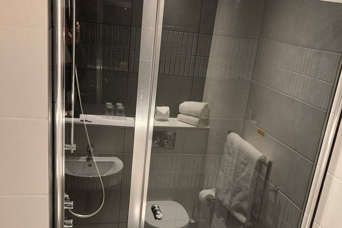 A glass-enclosed shower stall with a white bathtub, a toilet, and a towel rack.