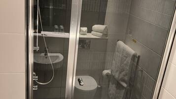 Cabina de ducha con paredes de vidrio, una bañera blanca, un inodoro y un perchero para toallas.