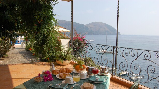 Una mesa lista para el desayuno, con vista al mar y a las montañas.