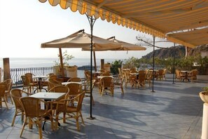 An outdoor café with wicker chairs and tables, umbrellas, and a view of the sea. - Giardino sul Mare (Lipari)