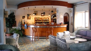 Una zona de bar con mobiliario de mimbre, suelo de baldosas y una barra llena de botellas.