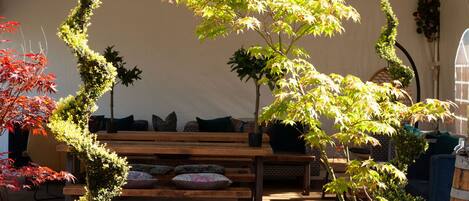A covered outdoor area with a wooden bench, potted plants, and a white tent.
