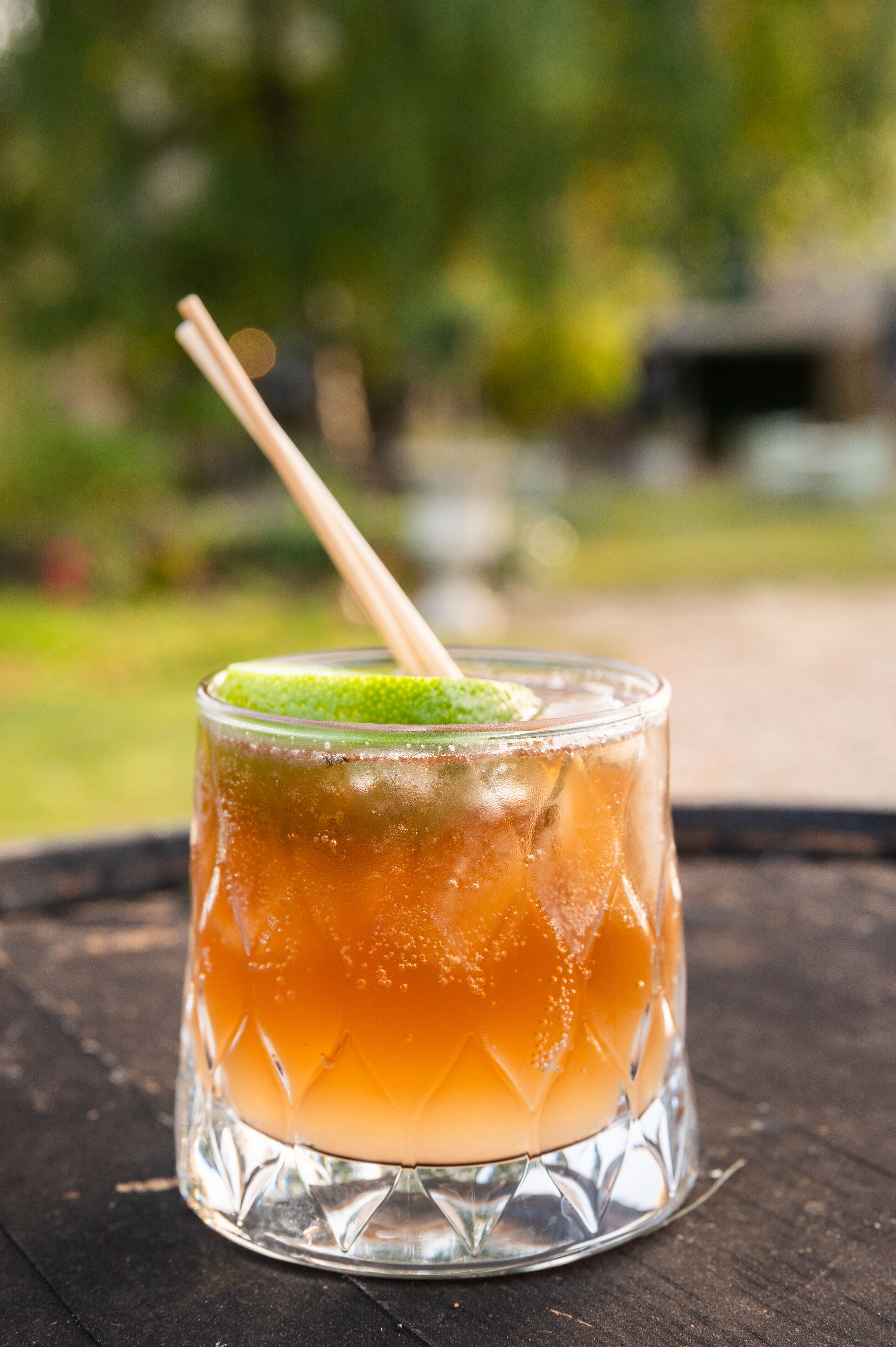 Un verre contenant une boisson à plusieurs couches, une tranche de citron vert et une paille, posé sur une surface en bois.