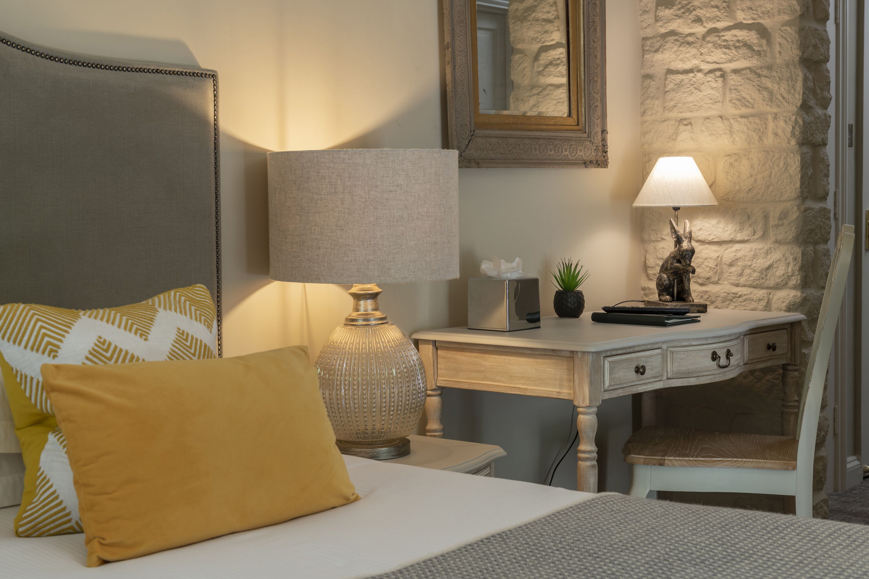 A neatly arranged bedroom with a bed, bedside table, lamp, and a small desk with a chair.
