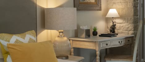 A neatly arranged bedroom with a bed, bedside table, lamp, and a small desk with a chair.