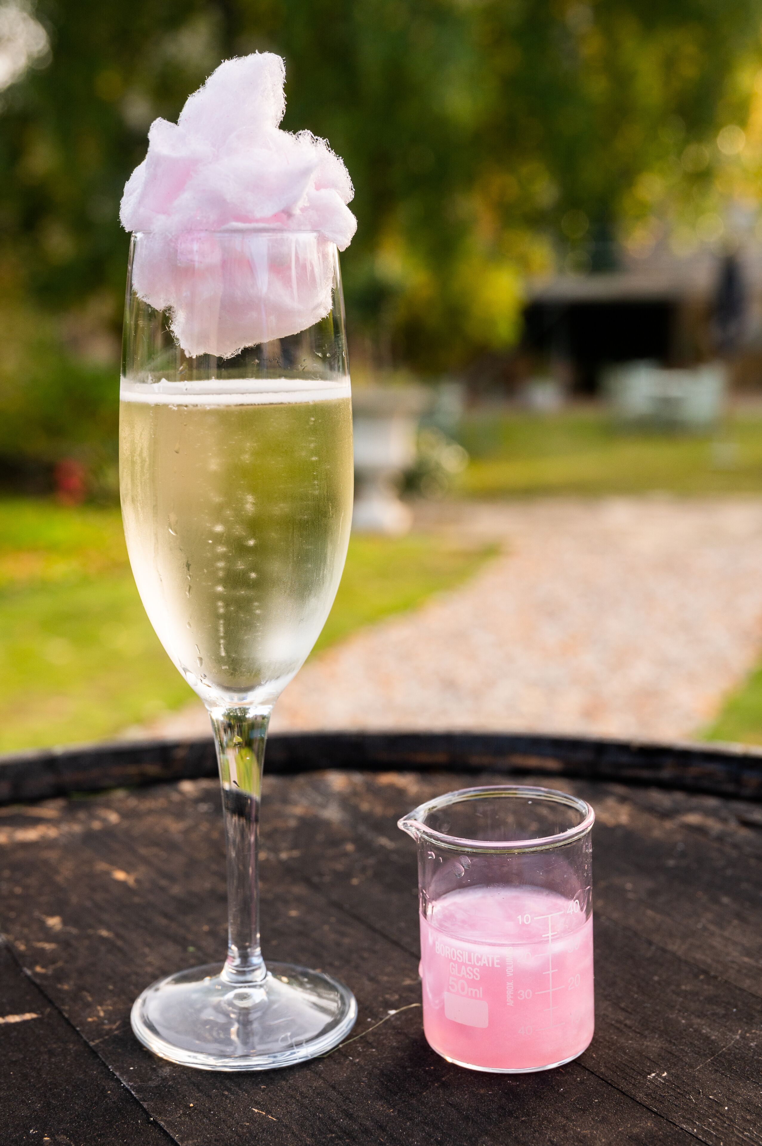 A glass of white beverage with a pink garnish on a wooden table outdoors.