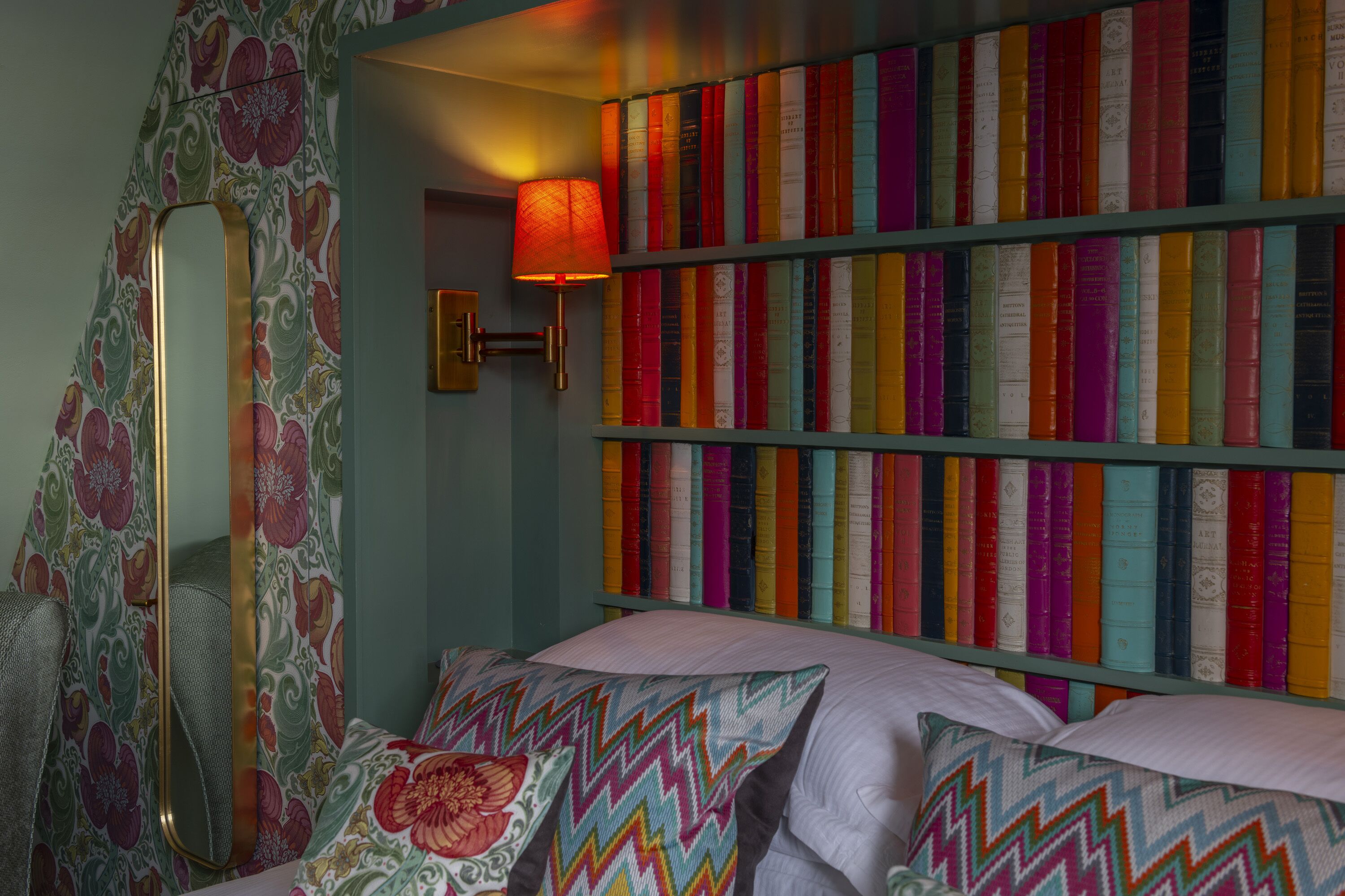 A bedroom with a bookshelf, a mirror, and a patterned wall.