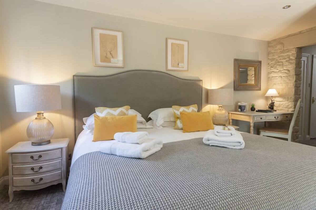 Quarto de hotel bem organizado, com uma cama grande, mesas de cabeceira, escrivaninha e uma parede de destaque em pedra.