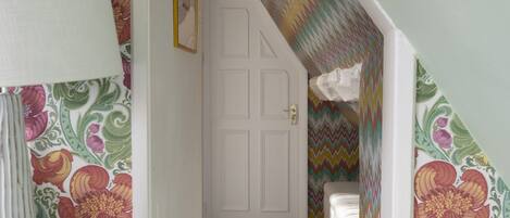 A narrow hallway with floral wallpaper, a white door, and a patterned wall.
