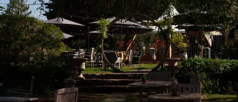 Een terras met houten tafels en stoelen, omringd door weelderig groen en bomen.