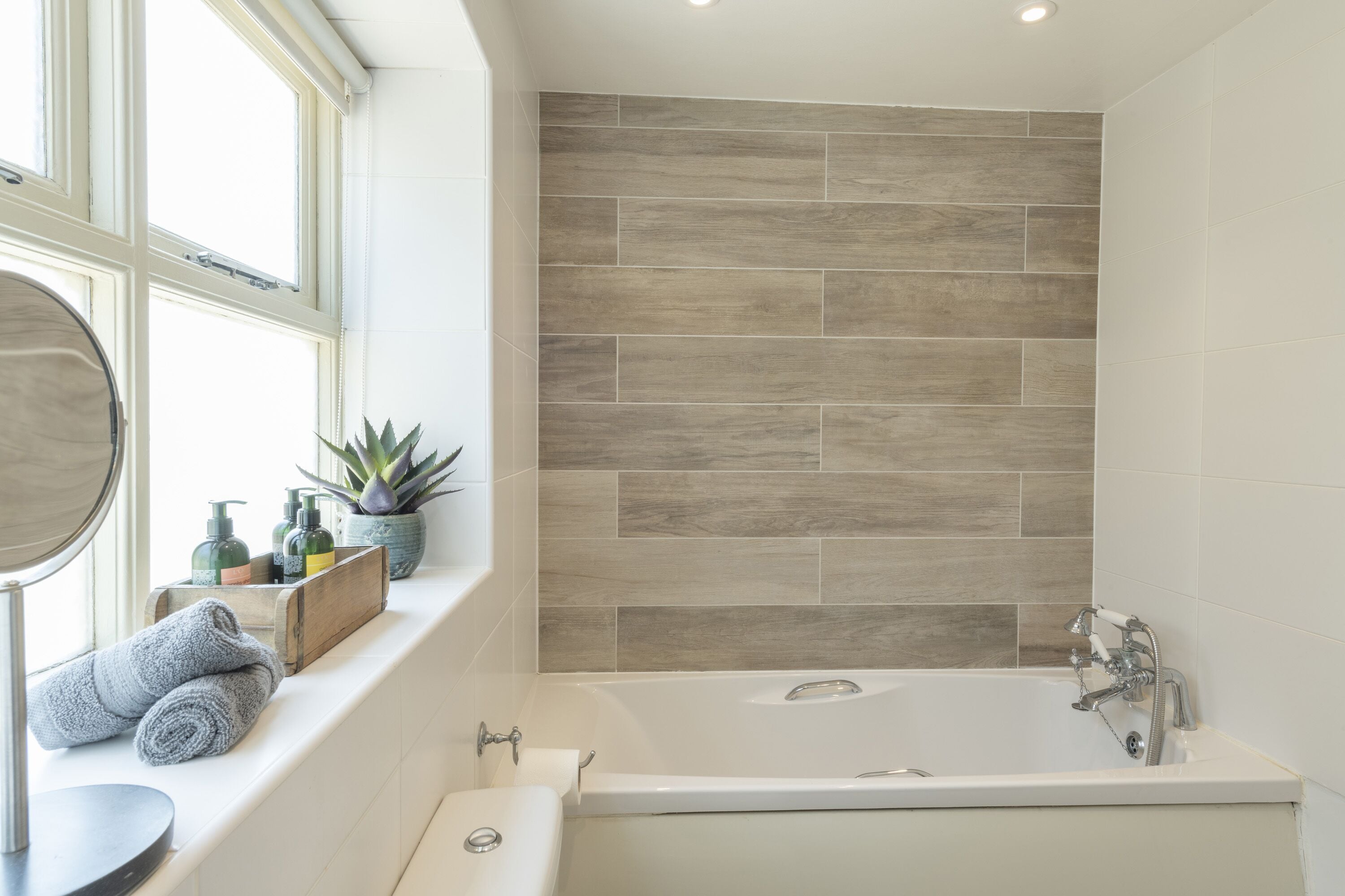A bathroom with a bathtub, a window with a view, and toiletries on the windowsill.