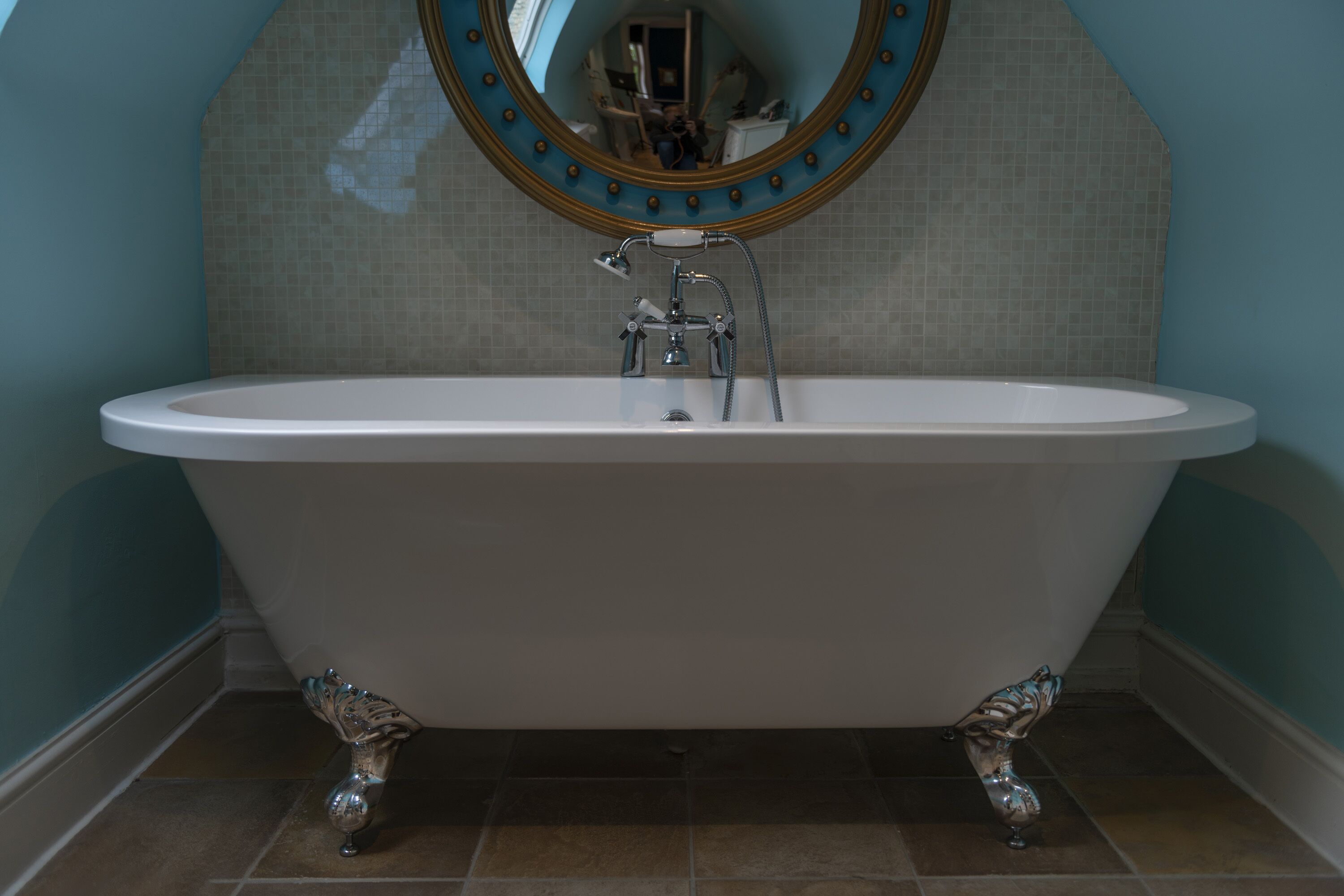 A freestanding bathtub with a showerhead, a wall-mounted mirror with a decorative frame, and a tiled floor.