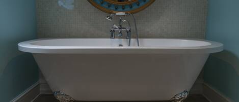 A freestanding bathtub with a showerhead, a wall-mounted mirror with a decorative frame, and a tiled floor.