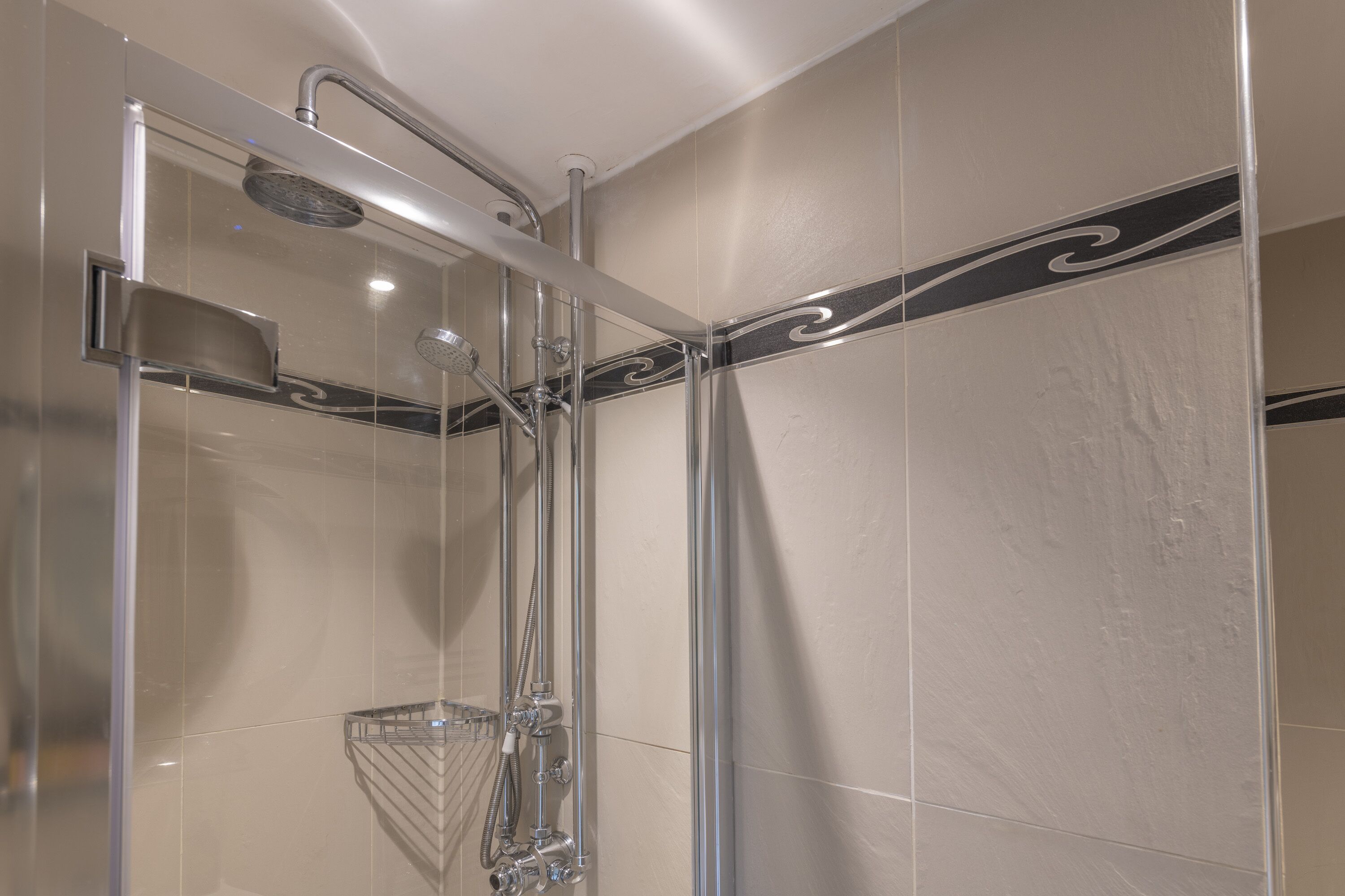 A modern shower with a glass enclosure, chrome fixtures, and a decorative black stripe on the wall.