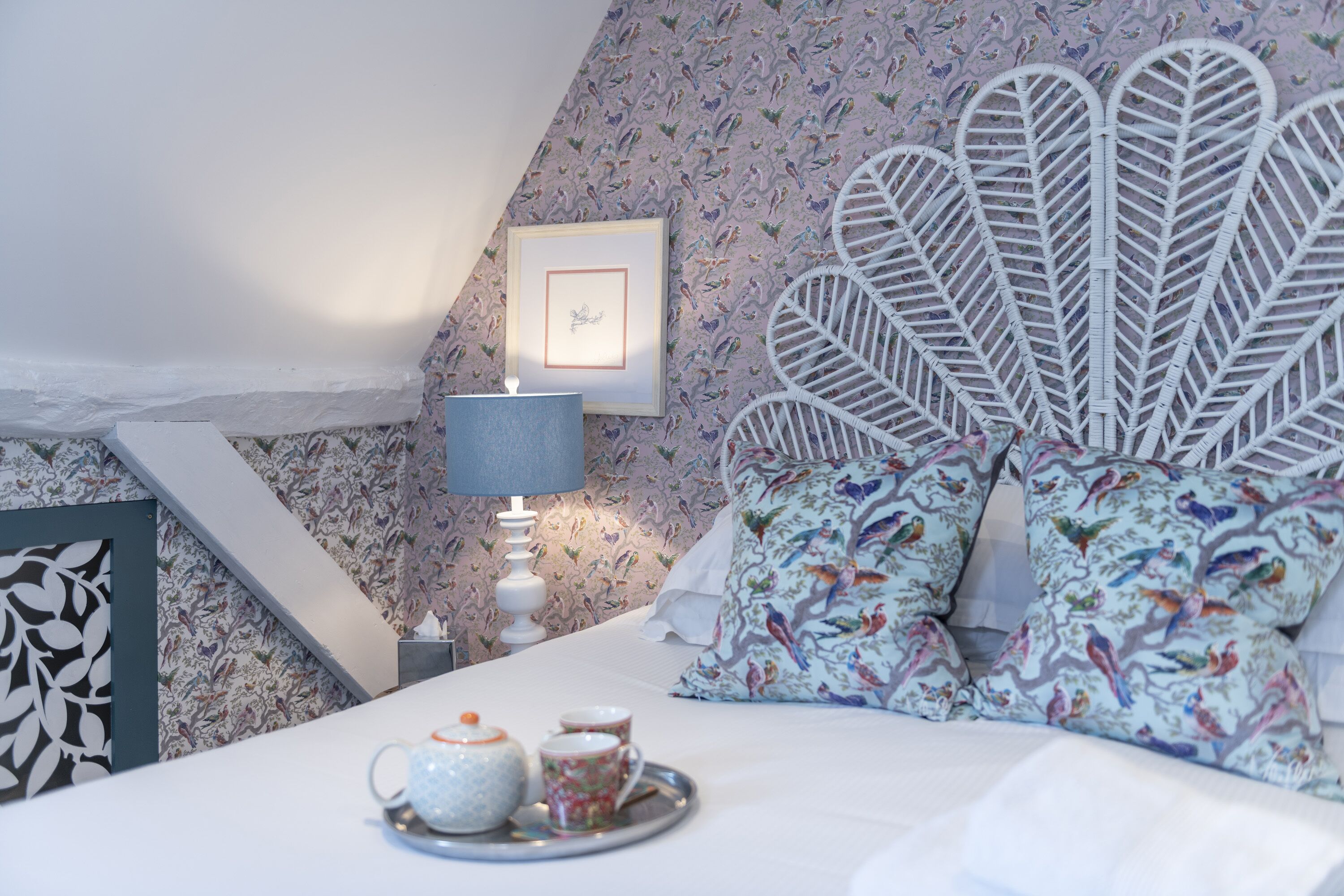 A bedroom with a bed, a nightstand, a lamp, and a tray with teacups.