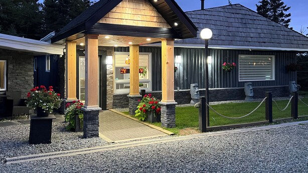 A building with a wooden facade, stone pillars, and a gravel driveway.