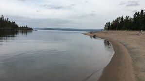 A calm lake with a sandy beach and dense forest on one side.