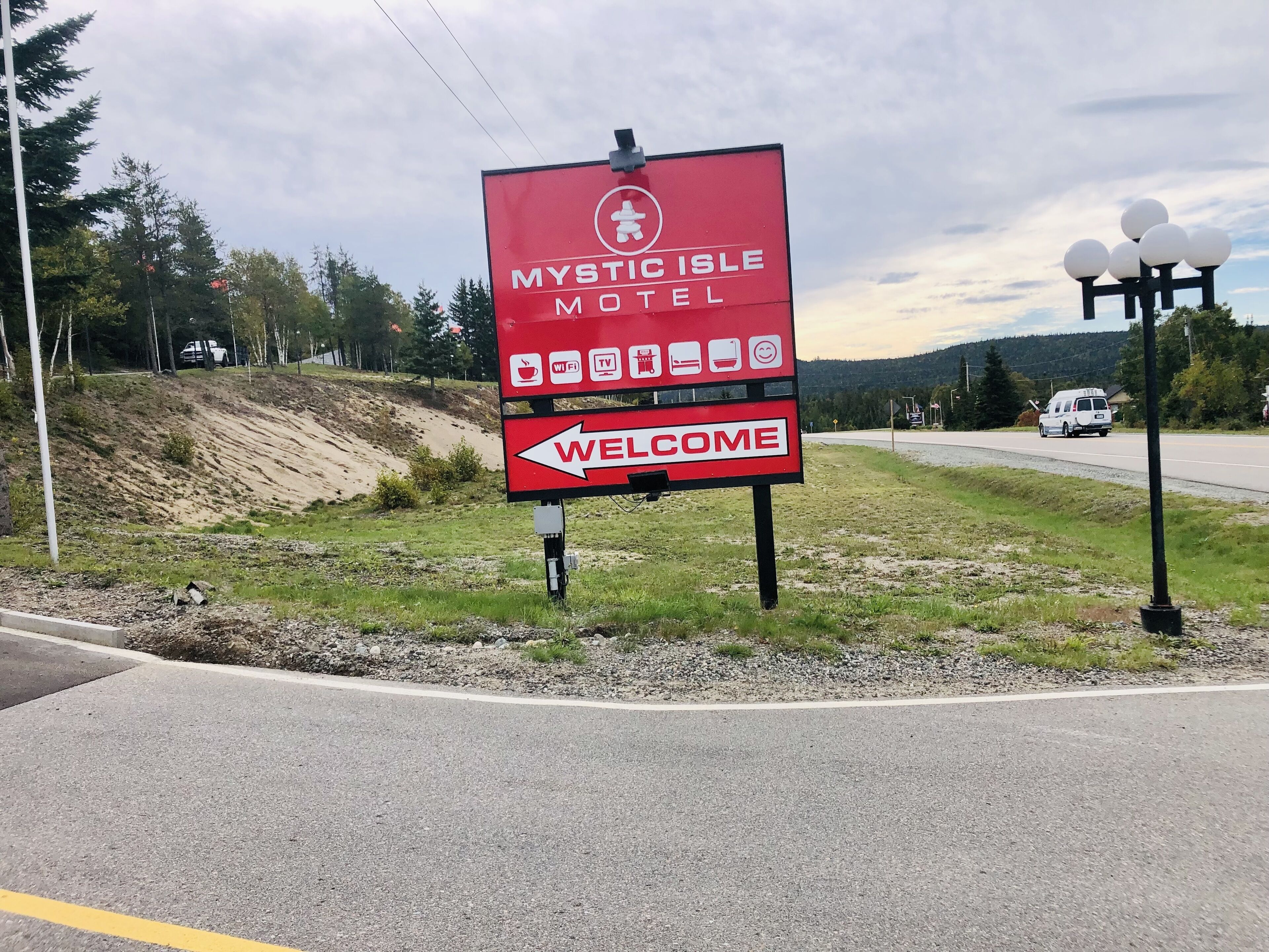 A welcome sign for Mystic Isle Motel with amenities icons and a directional arrow.