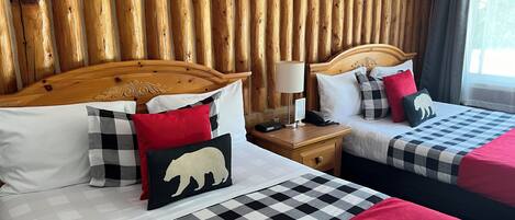 A hotel room with two beds, wooden paneling on the walls, a nightstand with a lamp, and a checkered bedspread.