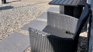 An outdoor seating area with wicker chairs and tables, a gravel path, and a sign indicating ice and beverages.