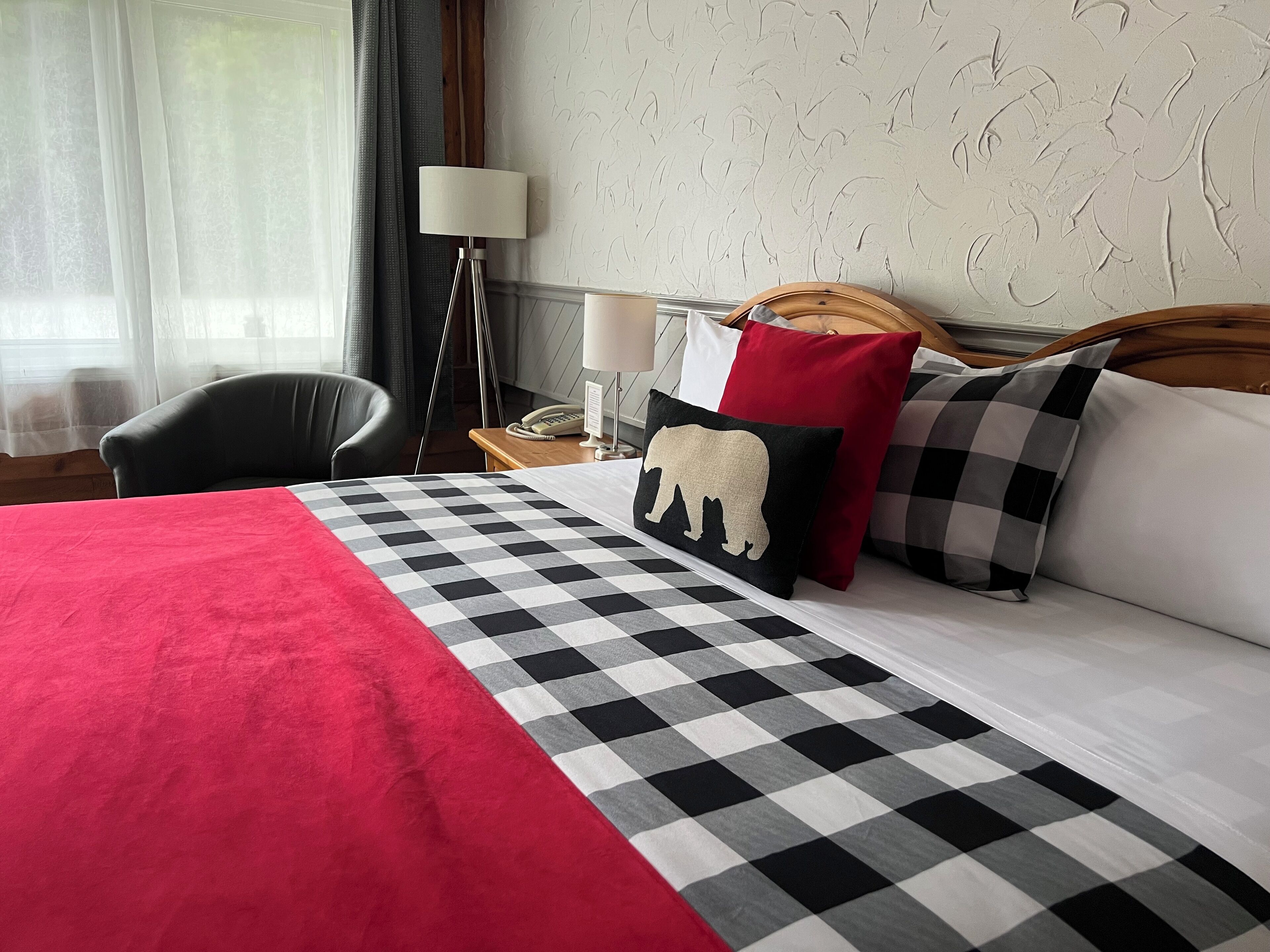 Una habitación de hotel con una colcha a cuadros, una manta roja, un cabecero de madera y una mesita de noche con una lámpara y un teléfono.