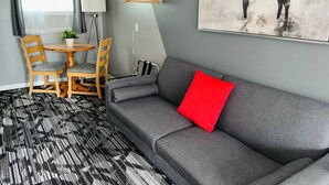 A modern living room with a grey sofa, a red pillow, a dining table with chairs, and a wall-mounted coat rack.