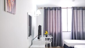 A hotel room with a bed, a desk with a chair, a television, and a window with curtains. - Hotel La Riviera (Santa Marta)