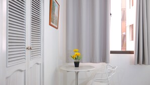 A room with a white door, a small table with a potted plant, a white chair, and a window with curtains. - Hotel La Riviera (Santa Marta)