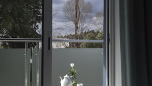 Un balcón con una mesa lista para tomar té, un pouf blanco y vistas a árboles y una estructura de madera.