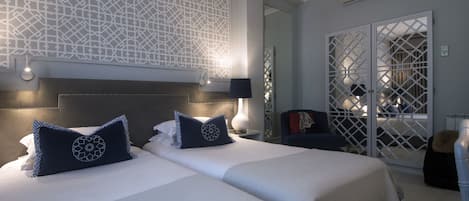 Ett hotellrum med två sängar, en dekorativ vägg, en sittgrupp och utsikt genom en glasdörr.