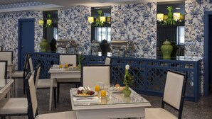 Un comedor con papel tapiz floral azul y blanco, un separador de vidrio y una mesa servida con desayuno.
