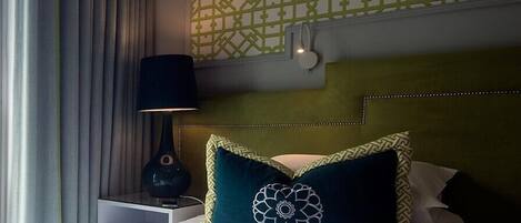 Una habitación de hotel con una cama bien hecha, una mesita de noche con una lámpara y un papel tapiz estampado.