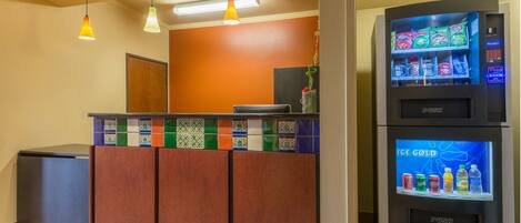 A reception area with a colorful tiled counter, a refrigerator stocked with beverages, and a small trash bin.