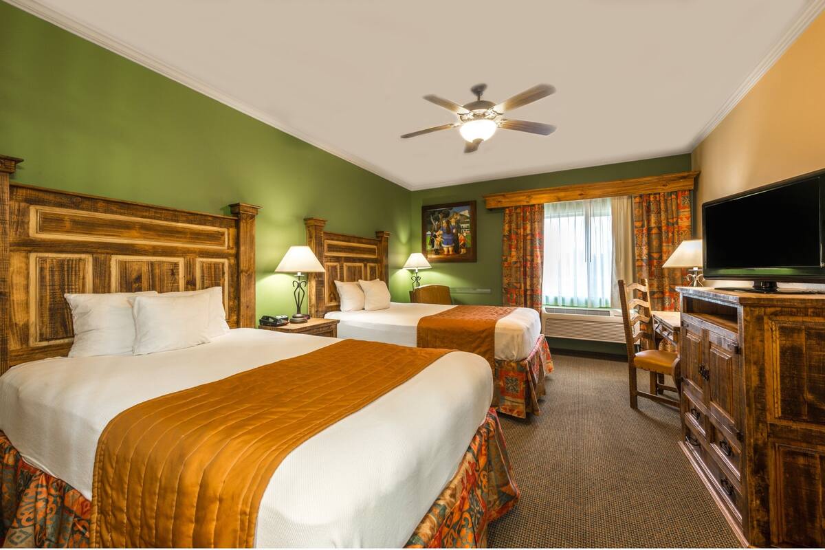 A hotel room with two beds, a television, a ceiling fan, and a window with curtains.