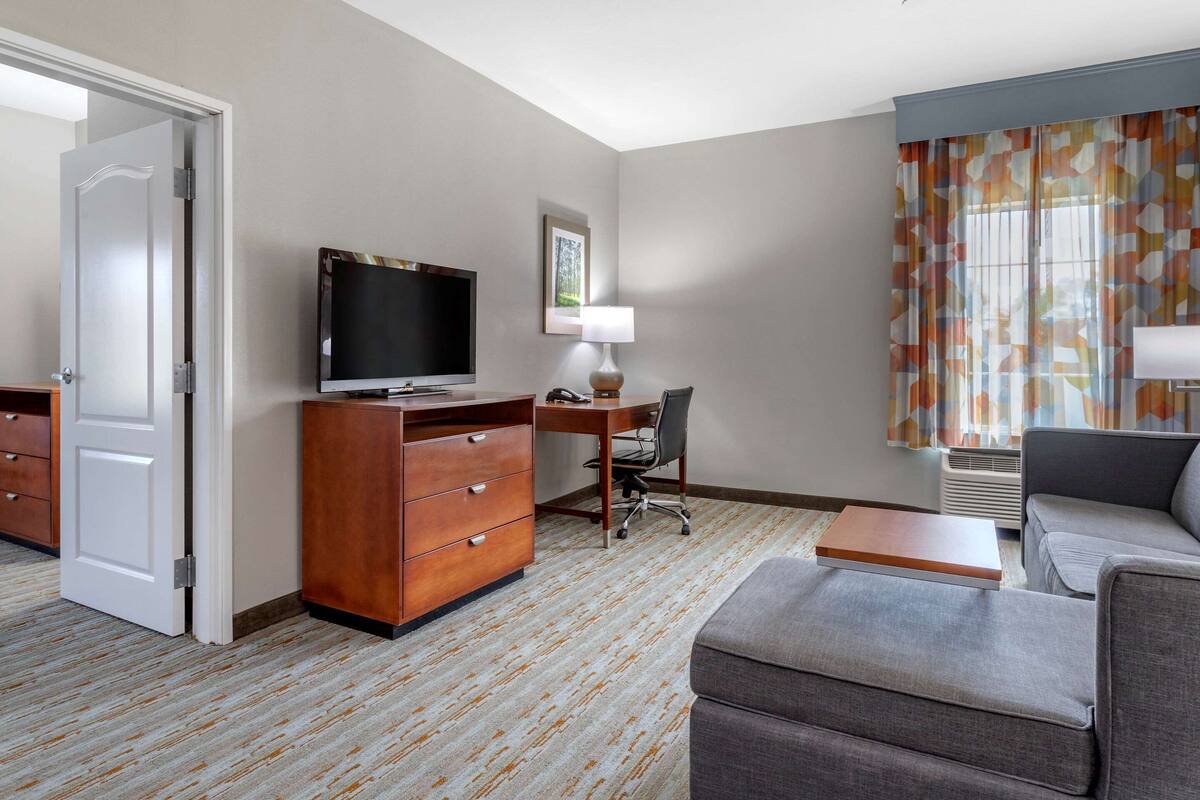 Une chambre d’hôtel équipée d’un bureau, d’une chaise, d’une télévision, d’un canapé et d’une fenêtre avec des rideaux.