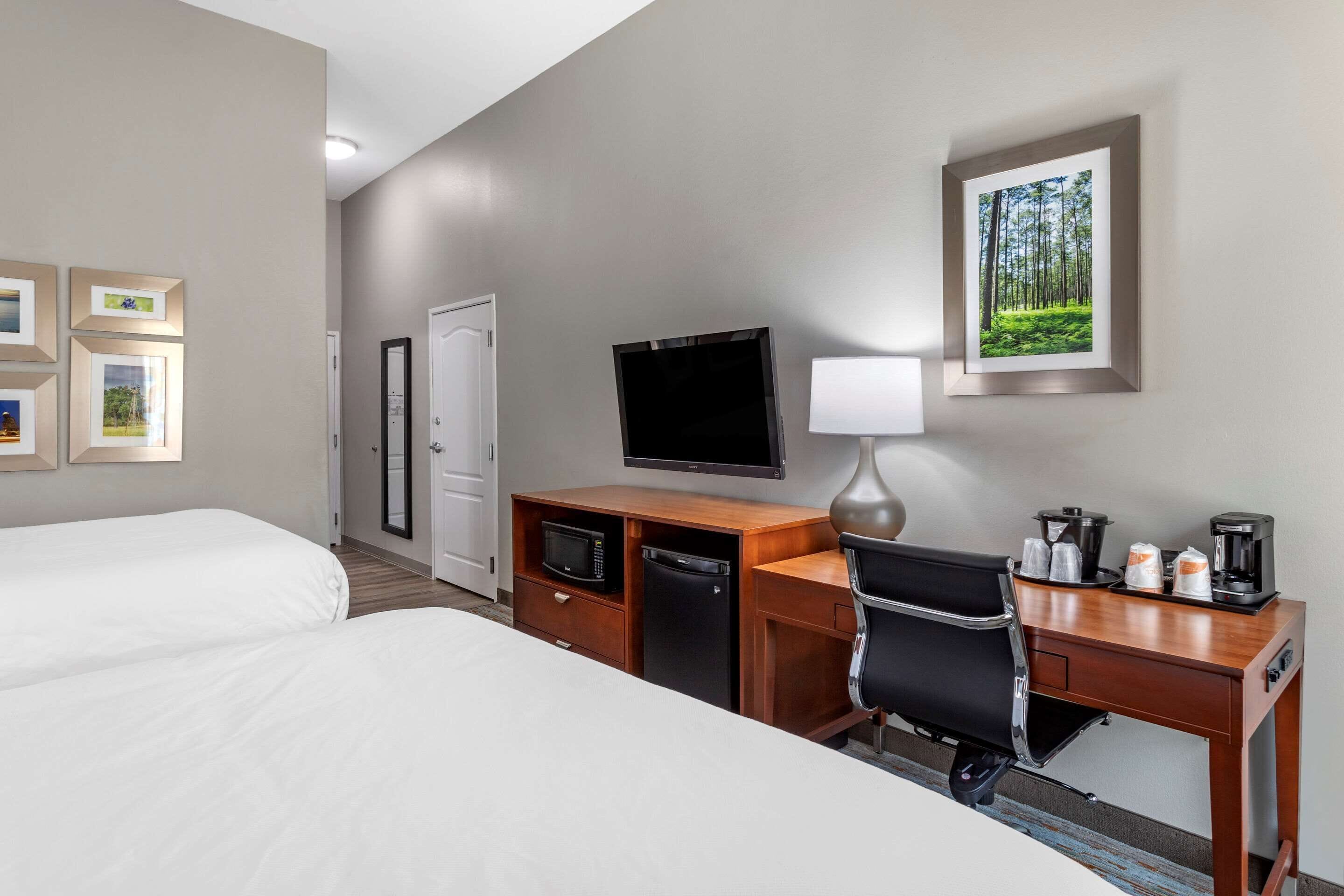 A hotel room with two beds, a desk with a chair, a television, a microwave, a coffee maker, and framed pictures on the wall.