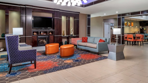 A modern living room with a flat-screen TV, comfortable seating, a fireplace, and a dining area with orange chairs. - Comfort Inn & Suites Cleveland TX (Cleveland)