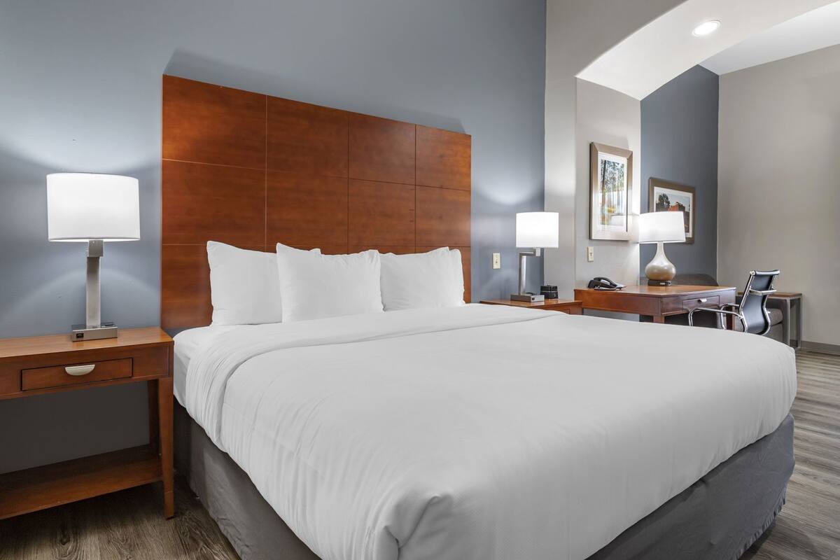 A hotel room with a large bed, two bedside tables with lamps, a desk with a chair, and a painting on the wall.