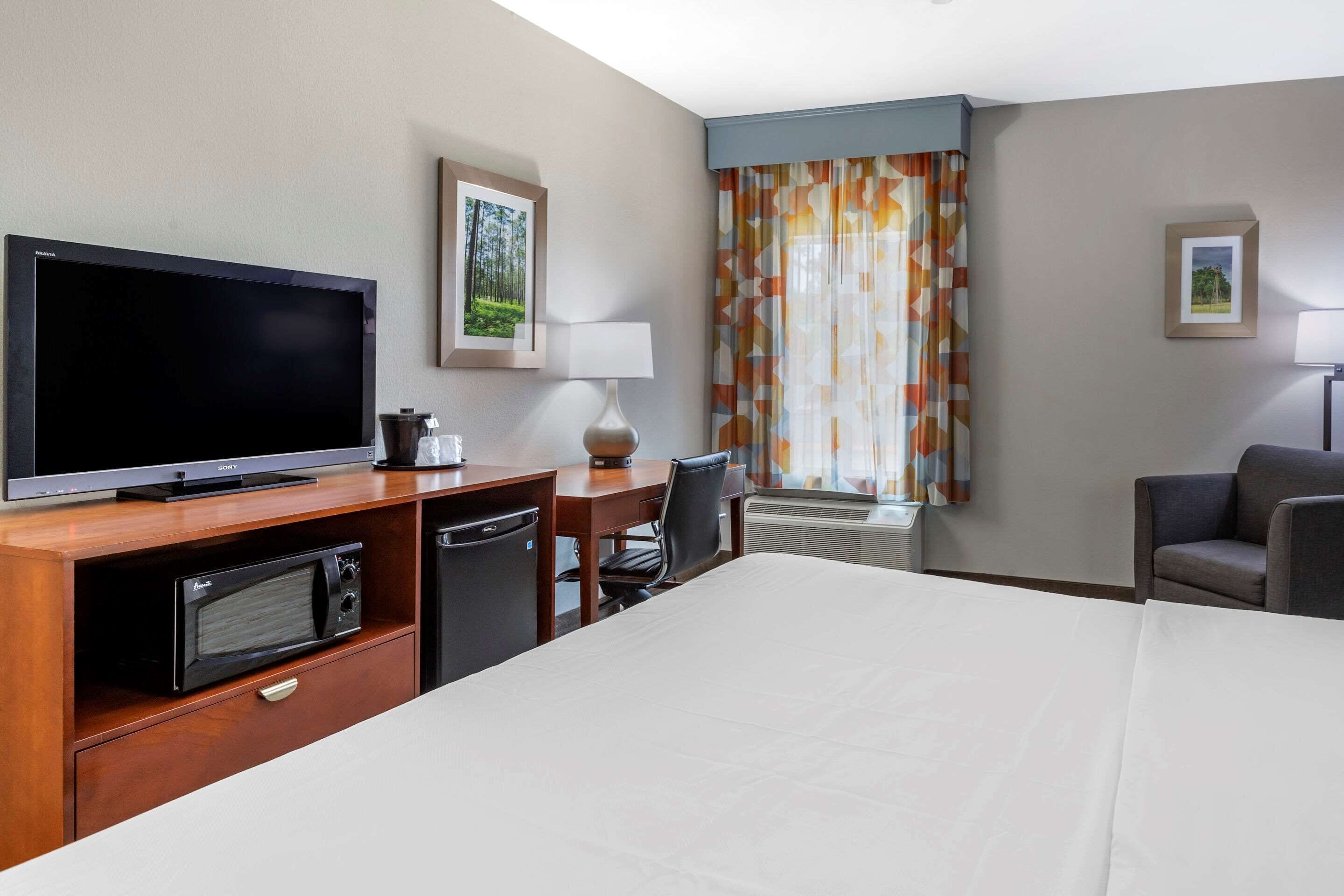 A hotel room with a bed, a TV, a desk with a lamp, a chair, and a microwave.