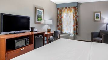 A hotel room with a bed, a TV, a desk with a lamp, a chair, and a microwave.