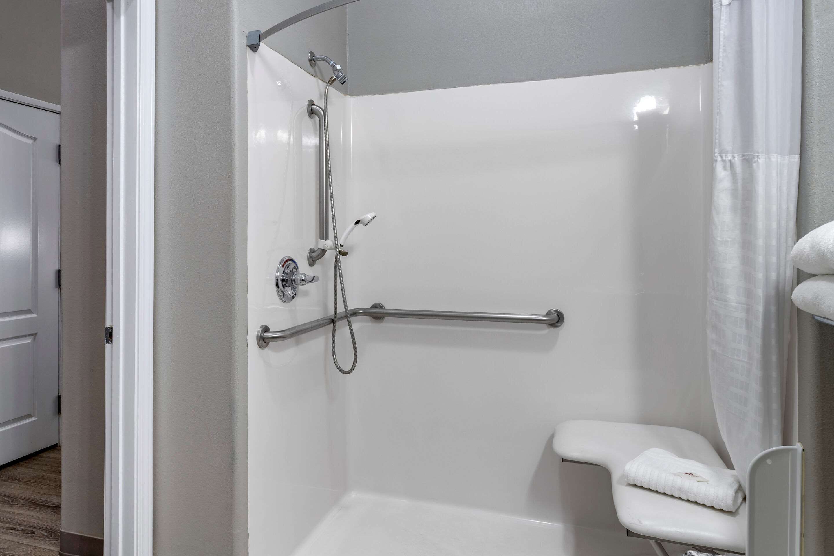 A modern bathroom with a walk-in shower, grab bar, and a white towel on the floor.