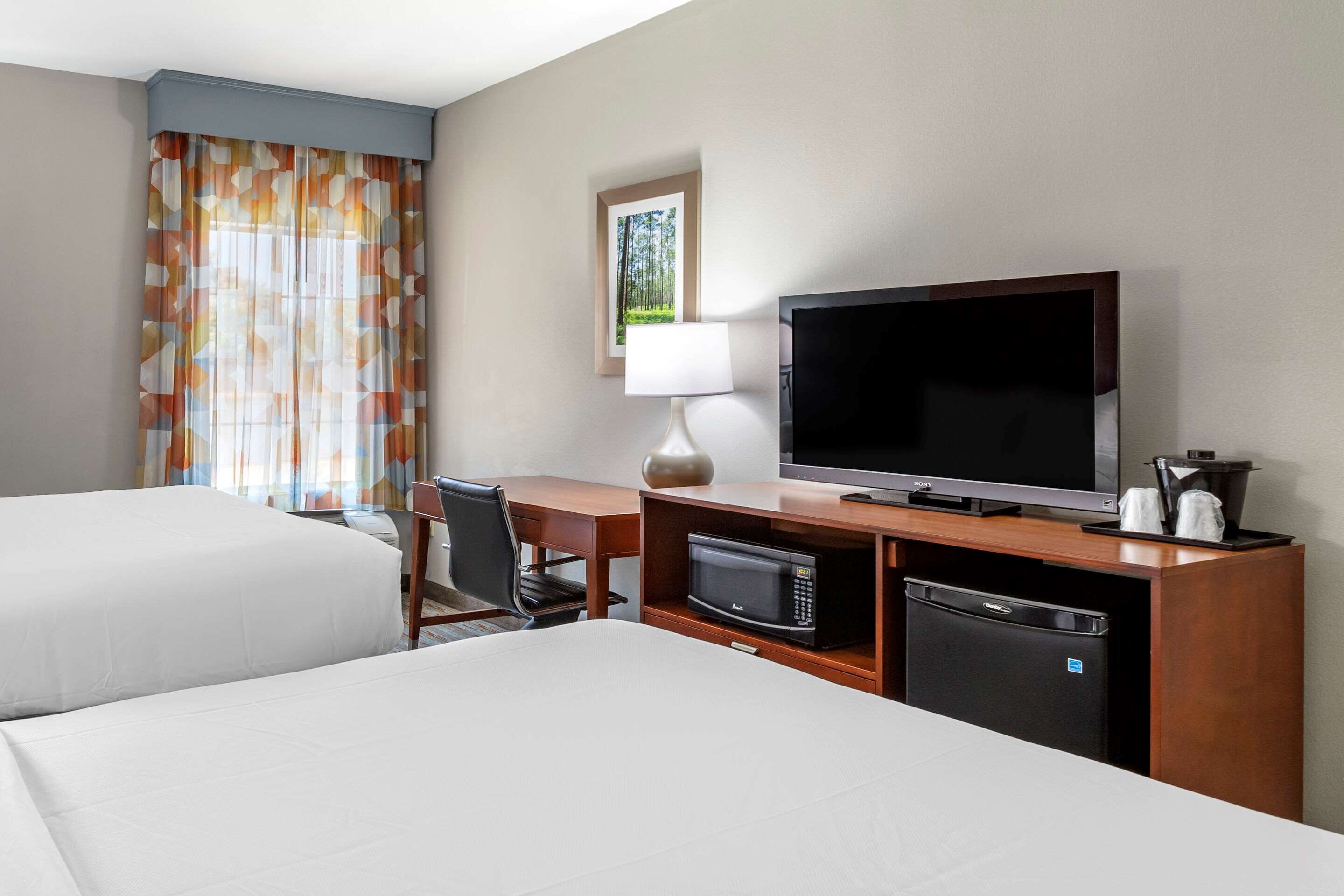 A hotel room with two beds, a TV, a desk with a lamp, a microwave, and a refrigerator.