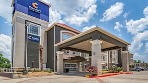 A Comfort Inn & Suites building with a prominent blue sign, a covered entrance, and a landscaped area with plants and flowers. - Comfort Inn & Suites Cleveland TX (Cleveland)
