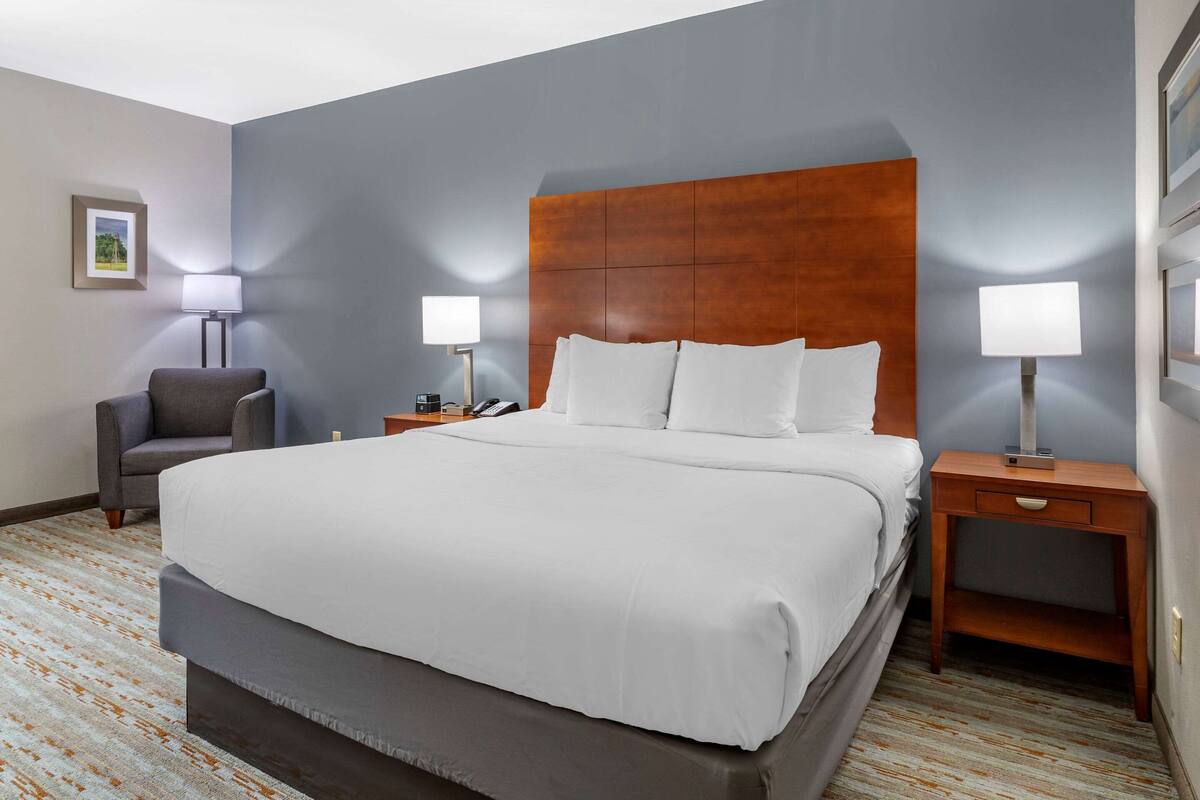 Une chambre d’hôtel avec un grand lit, deux tables de chevet, une chaise et une lampe.
